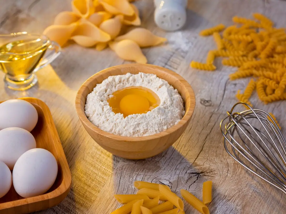 Ahşap tezgâhta un kâsesi, yumurta ve kuru makarna